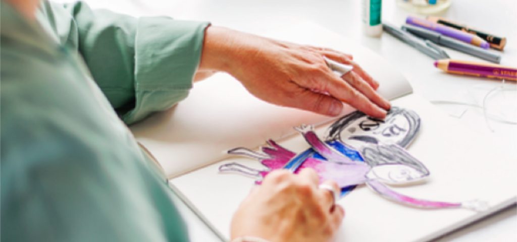 Zwei gezeichnete innere Anteile werden auf einem Papier zusammengelegt, Hände und Stifte sichtbar – kreative Biografiearbeit und Teile-Arbeit im Workshop